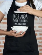 Delantal negro con la frase “Dios anda entre pucheros”, producto solidario de Have a God Time