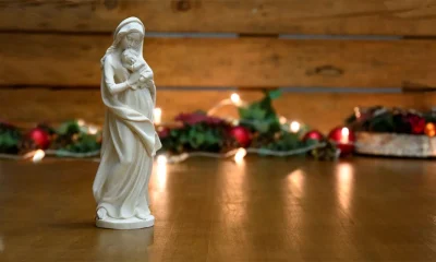 Figura de la Virgen con el Niño Jesús delante de luces de Navidad desenfocadas
