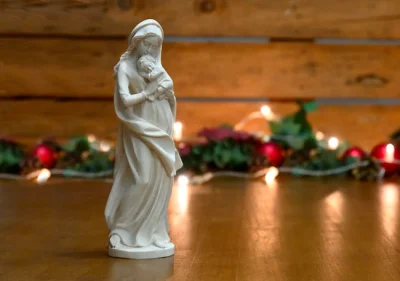 Figura de la Virgen con el Niño Jesús delante de luces de Navidad desenfocadas